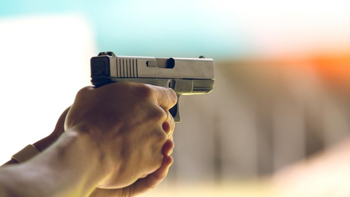 Hand aiming a pistol at a shooting range with flare and vintage tones