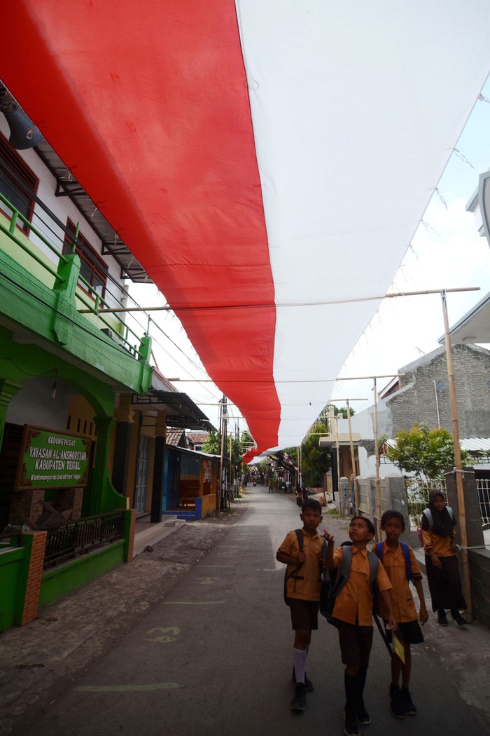 Sejumlah pelajar melintas dibawah bendera Merah Putih yang dibentangkan di atas jalan Desa Kademangaran, Kabupaten Tegal, Jawa Tengah, Jumat (2/8/2024). Bendera sepanjang 400 meter dan lebar tiga meter yang dijahit selama tiga bulan tersebut dipasang dalam rangka menyambut HUT ke-79 Kemerdekaan RI. ANTARA FOTO/Oky Lukmansyah/Spt.
