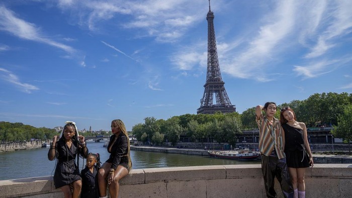 People pose for photographs near the Eiffel Tower at the 2024 Summer Olympics, Sunday, July 28, 2024, in Paris, France. (AP Photo/Yasin Dar)