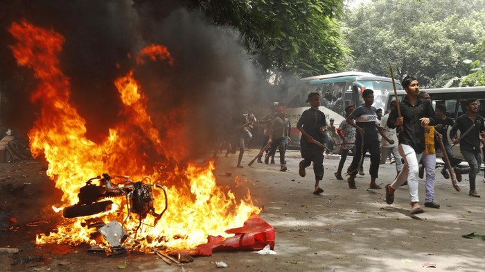 Men run past a shopping center which was set on fire by protesters during a rally against Prime Minister Sheikh Hasina and her government demanding justice for the victims killed in the recent countrywide deadly clashes, in Dhaka, Bangladesh, Sunday, Aug. 4, 2024. (AP Photo/Rajib Dhar)