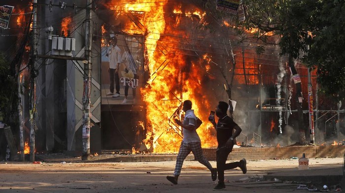 Men run past a shopping center which was set on fire by protesters during a rally against Prime Minister Sheikh Hasina and her government demanding justice for the victims killed in the recent countrywide deadly clashes, in Dhaka, Bangladesh, Sunday, Aug. 4, 2024. (AP Photo/Rajib Dhar)
