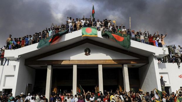 Demonstran antipemerintah mengibarkan bendera nasional Bangladesh saat menyerbu istana Perdana Menteri Sheikh Hasina di Dhaka pada 5 Agustus 2024. (AFP/K M ASAD)