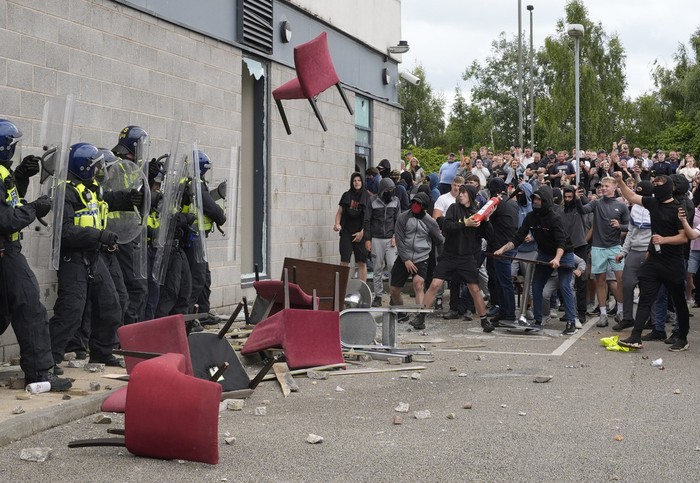 A chair is thrown at police officers as trouble flares during an anti-immigration protest outside the Holiday Inn Express in Rotherham, England, Sunday Aug. 4, 2024. (Danny Lawson/PA via AP)