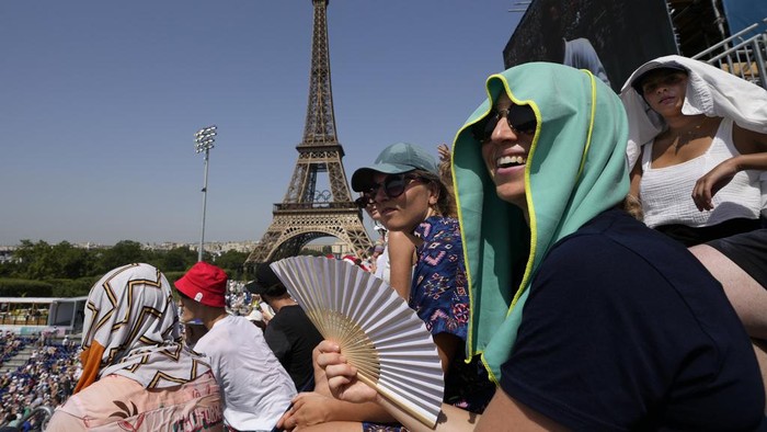 Stephanie Touissaint, foreground, uses a fan to keep cool in the sweltering heat at Eiffel Tower Stadium during a beach volleyball match between Cuba and Brazil at the 2024 Summer Olympics, Tuesday, July 30, 2024, in Paris, France. (AP Photo/Robert F. Bukaty)