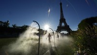 Penonton berjalan melalui penyemprot kabut air dalam perjalanannya ke Stadion Menara Eiffel untuk menonton bola voli pantai. Di beberapa wilayah Prancis selatan, suhunya bahkan mencapai 41 derajat Celcius. AP/Robert F. Bukaty