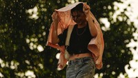 Seorang wanita ini melindungi tubuhnya dari guyuran hujan dengan menggunakan baju.