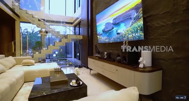 Unsur kayu mendominasi eksterior hingga interior rumah. Pintu depan saja terbuat dari kayu merbau Papua yang kokoh. Di ruang keluarga, elemen kayu menciptakan atmosfer yang hangat. (Foto: YouTube/Trans7 Official)