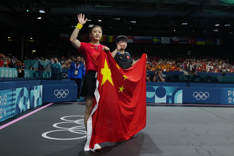 Gold medalist China's Chen Meng, foreground, and silver medalist China's Sun Yingsha pose with the flag of their country after the women's singles table tennis match at the 2024 Summer Olympics, Saturday, Aug. 3, 2024, in Paris, France. (AP Photo/Petros Giannakouris)