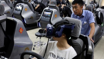 Seorang instruktur mengemudi memandu seorang siswa berlatih pada simulator mengemudi mobil realitas virtual (VR) di Eastern Pioneer Driving School di Beijing, China.  