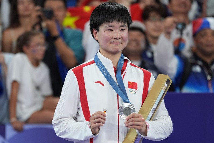 PARIS, FRANCE - AUGUST 05: Chinas silver medalist He Bingjiao celebrates on the podium during the medal ceremony after the Badminton - Womens Singles Gold Medal Match on day ten of the Paris 2024 Olympic Games at Porte de La Chapelle Arena on August 5, 2024 in Paris, France. (Photo by Nin Minzhe/CHINASPORTS/VCG via Getty Images)