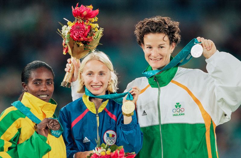 SYDNEY, AUSTRALIA - SEPTEMBER 25: Gabriela Szabo of Romania showing her gold medal with Sonia O'Sullivan of Ireland in 2nd place and Gete Wami of Ethiopia in 3rd place during the medal ceremony for the Women's 5000m Final during the Sydney 2000 Olympic Games at the Olympic Stadium on September 25th, 2000 in Sydney, Australia. (Photo by Simon Bruty/Anychance/Getty Images)