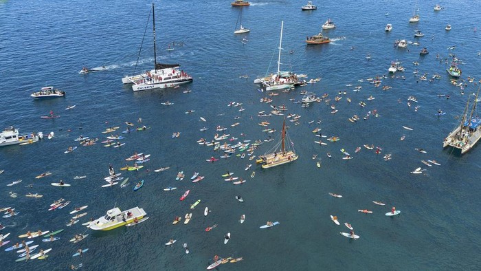 Dalam memperingati satu tahun kebakaran hutan Lahaina di Hawaii, sejumlah warga melakukan aksi mendayung dan berselancar di laut lepas Lahaina. Ini potretnya.