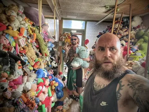 Mitch Johnson dan Jake Parr berfoto di antara tumpukan boneka