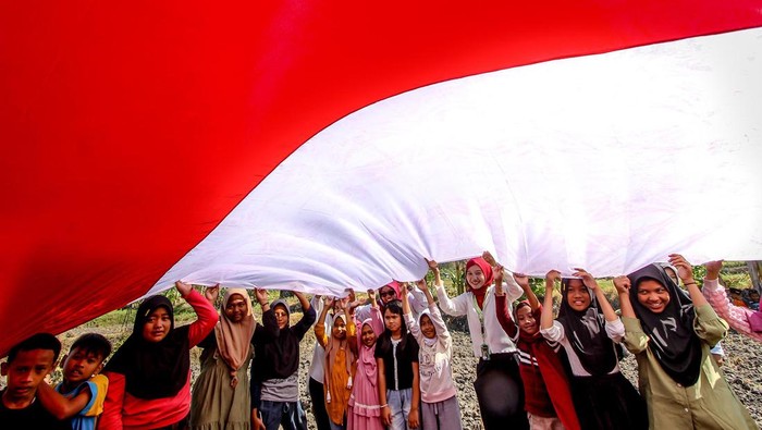 Sejumlah anak membentangkan bendera Merah Putih saat mengikuti kegiatan Sapa Desa di Ngluyu, Nganjuk, Jawa Timur, Minggu (11/8/2024). Aksi membentangkan bendera Merah Putih di salah satu daerah pelosok di Nganjuk tersebut merupakan bentuk upaya pemuda setempat untuk menanamkan semangat kemerdekaan dan cinta tanah air kepada masyarakat khususnya anak-anak di desa itu. ANTARA FOTO/Muhammad Mada/foc.