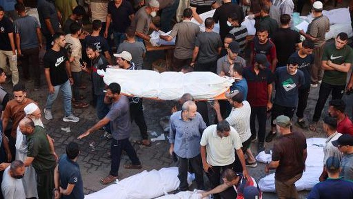 People carry away a shrouded body from the al-Maamadani hospital for burial, following an Israeli strike that killed more than 90 people on a school sheltering displaced Palestinians in Gaza City on August 10, 2024, amid the ongoing conflict between Israel and the Hamas movement. The Israeli military said it struck a Hamas 