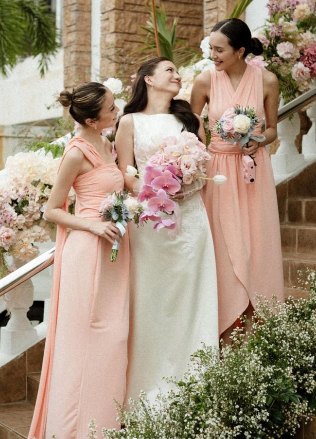 Cassandra tampil cantik dan simpel mengenakan gaun pengantin tanpa lengan berwarna putih. Rambutnya pun hanya diikat setengah dan dibuat bergelombang. Dalam foto tampak ia bersama kedua bridesmaidnya yang mengenakan dress berwarna peach. Foto: Instagram/@cassandraslee