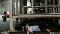 Seorang warga beristirahat di bawah halte bus yang rusak.