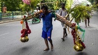 Seorang penganut Hindu membawa dua kendi besar berisi air suci dari Sungai Hooghly untuk dipersembahkan di kuil dewa Hindu Shiva selama Sawan Somwar.