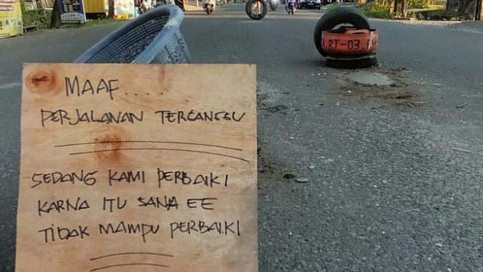 Jalan berlubang yang ditambal oleh warga di Jalan Cakalang, Kota Palopo dan dipasangi papan peringatan.