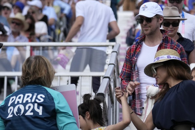 Ryan terlihat memakai kaus putih yang dibungkus kemeja merah kotak-kotak. Gaya aktor asal Kanada itu juga dilengkapi kacamata hitam dan topi baseball berlogo Olimpiade. Sementara itu, Eva Mendes memilih dress biru navy, juga dipadu topi dan kacamata. (Foto: AP/Mosaab Elshamy)