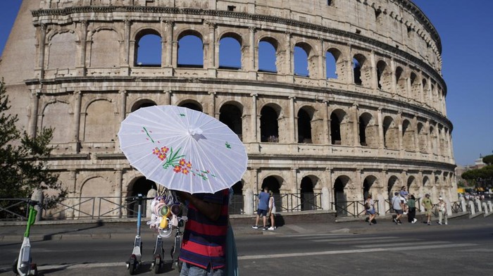 A man sells umbrellas and portable mini fans in front of the Colosseum as temperatures are expected to reach up to 39 degrees Celsius (102.20 Fahrenheit) in Rome, Saturday, Aug. 10, 2024. (AP Photo/Gregorio Borgia)
