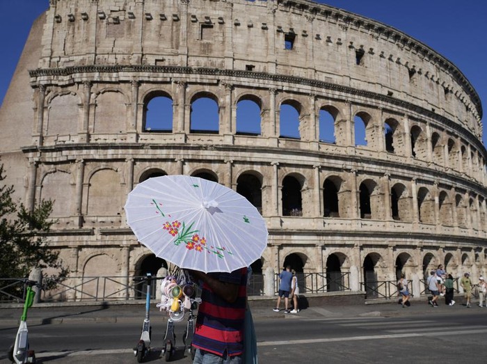 A man sells umbrellas and portable mini fans in front of the Colosseum as temperatures are expected to reach up to 39 degrees Celsius (102.20 Fahrenheit) in Rome, Saturday, Aug. 10, 2024. (AP Photo/Gregorio Borgia)
