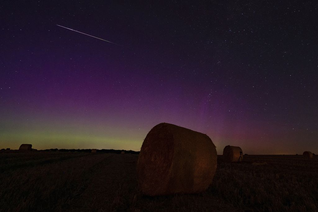 Aura warna-warni bersinar di balik tumpukan jerami sementara bintang jatuh dari hujan meteor Perseid terbakar di langit Berlin, Jerman, Senin malam, 12 Agustus 2024. (Georg Moritz/dpa via AP)