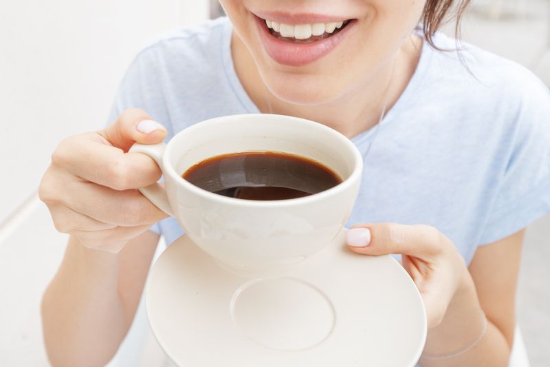 Happy woman drinks a black espresso coffee and smiles. The concept of problems with the color of teeth from bad habits