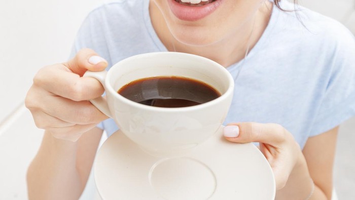 Happy woman drinks a black espresso coffee and smiles. The concept of problems with the color of teeth from bad habits