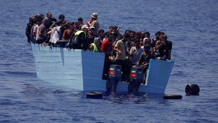 Migrants stand on a wooden boat near NGO Open Arms rescue boat 