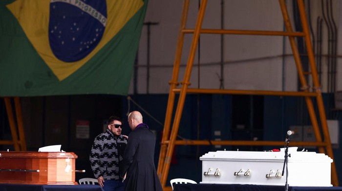 A priest talks to relatives of victims of the airplane crash that killed 62 people, during a tribute, before the coffins are delivered to their hometown, in Guarulhos, Brazil, August 13, 2024. REUTERS/Carla Carniel