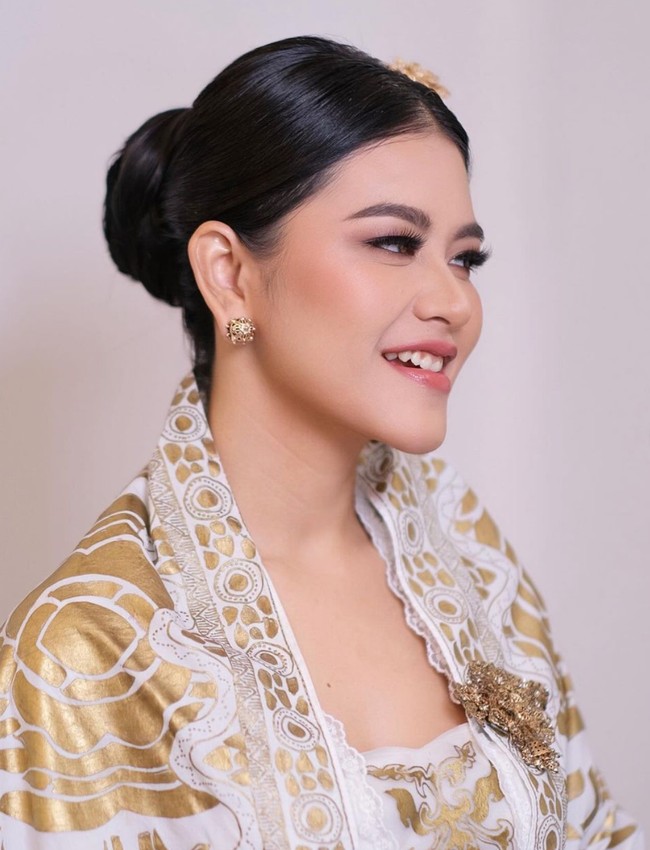 Dalam beberapa foto yang dibagikan terlihat Kahiyang mengenakan busana berwarna putih dipenuhi dengan aksen gold rancangan Era Soekamto. Pada bagian dada sebelah kirinya ia juga menambahkan bros berwarna gold untuk mempermanis tampilannya. Foto: Instagram/@malvava/@ayanggkahiyang