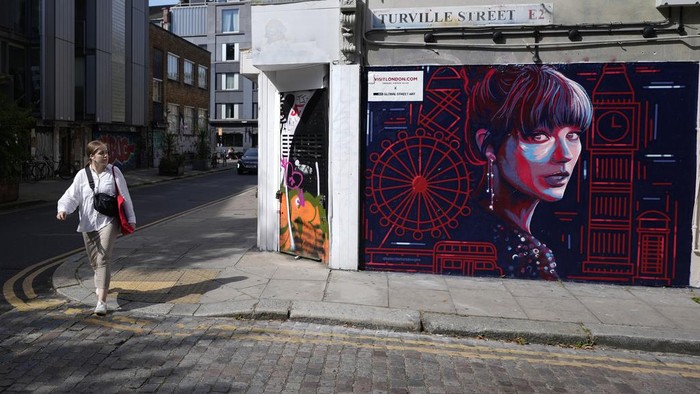 A new mural portrait of Taylor Swift designed by Kate Clayton, who poses next to it, as it is unveiled in Shoreditch in east London, Tuesday, Aug. 13, 2024. (AP Photo/Alastair Grant)
