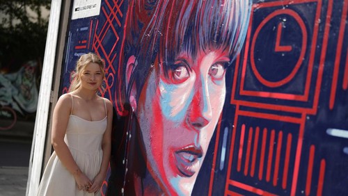 A new mural portrait of Taylor Swift designed by Kate Clayton, who poses next to it, as it is unveiled in Shoreditch in east London, Tuesday, Aug. 13, 2024. (AP Photo/Alastair Grant)