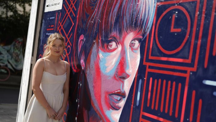 A new mural portrait of Taylor Swift designed by Kate Clayton, who poses next to it, as it is unveiled in Shoreditch in east London, Tuesday, Aug. 13, 2024. (AP Photo/Alastair Grant)