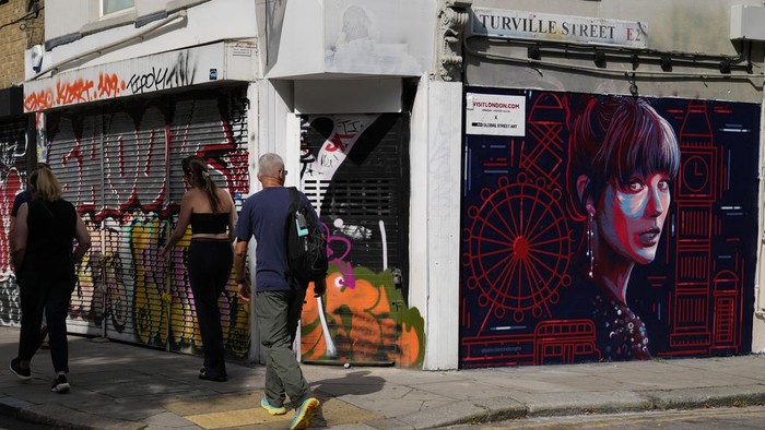 A new mural portrait of Taylor Swift designed by Kate Clayton, who poses next to it, as it is unveiled in Shoreditch in east London, Tuesday, Aug. 13, 2024. (AP Photo/Alastair Grant)