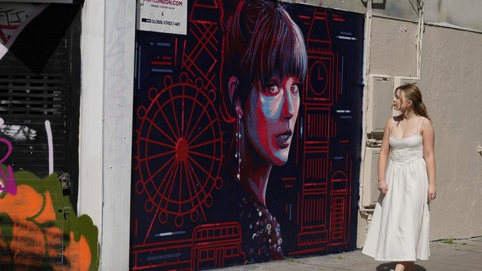 A new mural portrait of Taylor Swift designed by Kate Clayton, who poses next to it, as it is unveiled in Shoreditch in east London, Tuesday, Aug. 13, 2024. (AP Photo/Alastair Grant)