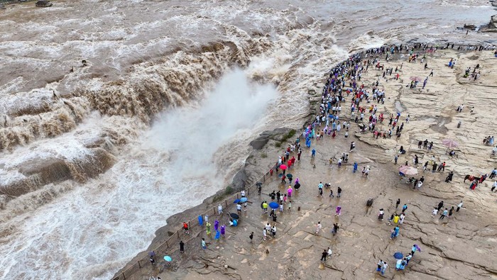 YAN'AN, CHINA - AUGUST 15: Tourists watch a roaring torrent carry a large amount of yellow sediment at the Hukou Waterfall on the Yellow River on August 15, 2024 in Yan'an, Shaanxi Province of China. (Photo by VCG/VCG via Getty Images)