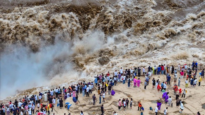 Aliran Air Terjun Hukou di China Jadi Tontonan, Bak Air Bah YAN'AN, CHINA - AUGUST 15: Tourists watch a roaring torrent carry a large amount of yellow sediment at the Hukou Waterfall on the Yellow River on August 15, 2024 in Yan'an, Shaanxi Province of China. (Photo by VCG/VCG via Getty Images)