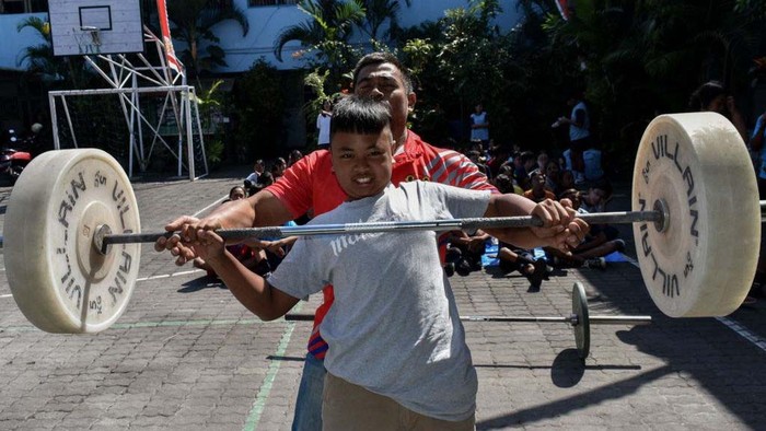 An athlete (in a red t-shirt) is teaching basic weightlifting techniques to students at SMP Petra Malang (Junior High School) in East Java, Indonesia, on August 15, 2024. The Road Show Weightlifting sports event is visiting several schools to find new athletes after Indonesia won the weightlifting gold medal at the 2024 French Olympics. (Photo by Aman Rochman/NurPhoto via Getty Images)