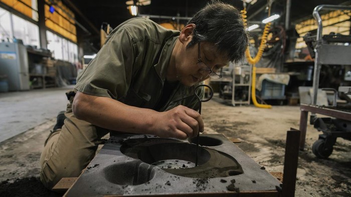 Workers prepare cast iron pots to put into a kiln to bake them with high temperature to make them rust resistant at the Oigen foundry in Oshu, northeastern Japan, Thursday, May 16, 2024. (AP Photo/Hiro Komae)