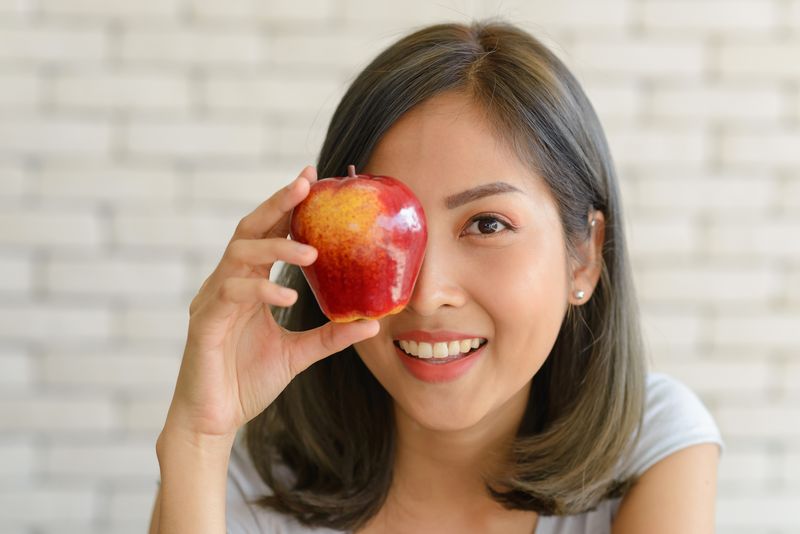 Portrait of Smiling Beautiful Young Asian Woman Holding Red Apple. close up