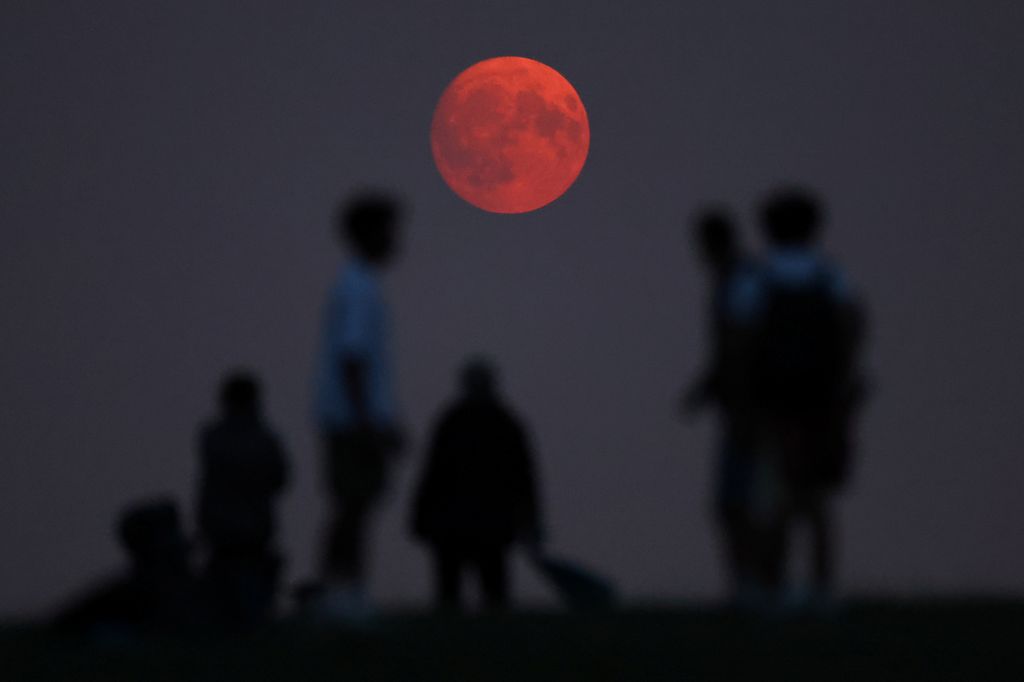 Orang-orang melihat bulan saat terbit, dengan cahaya merah yang disebabkan oleh partikel asap yang terbawa di atmosfer atas dari kebakaran hutan Amerika Utara, sehari sebelum bulan purnama super, di Parliament Hill di London, Inggris, 18 Agustus 2024. (REUTERS/Toby Melville)