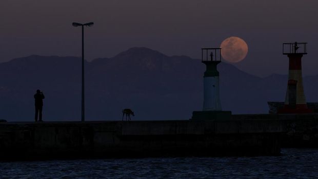 Seorang laki-laki mengambil foto bulan super, nan dikenal sebagai Bulan Biru, saat terbit di atas mercusuar di pelabuhan Kalk Bay di Cape Town, Afrika Selatan, 19 Agustus 2024. (REUTERS/Esa Alexander)