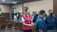 Tangannya terlihat diborgol dan ia pun mengenakan rompi tahanan berwarna merah.