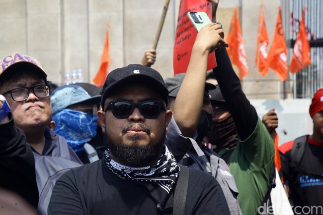Rigen mengandalkan kaus hitam dan topi senada, dengan scarf monokrom. (Foto: Ari Saputra/detikcom)
