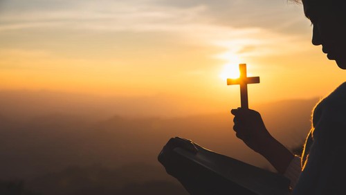 Wanita sedang memegang salib di gunung.