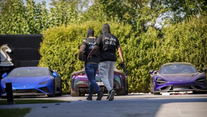 Deretan Mobil Mewah Disita dari Rumah Influencer Kontroversial Andrew Tate Masked police officers walk backdropped by sports cars at Andrew Tate's residence on the outskirts of Bucharest, Romania, Saturday, Aug. 24, 2024. (AP Photo/Vadim Ghirda)