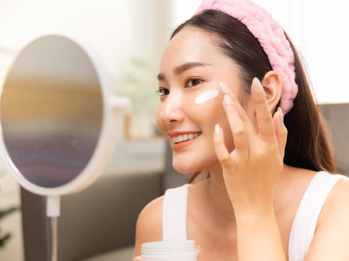 Mirror reflection of woman with skincare cream, spa lotion or dermatology ointment for melasma or acne treatment. Bathroom facial routine, healthcare and face of girl apply cosmetics beauty product