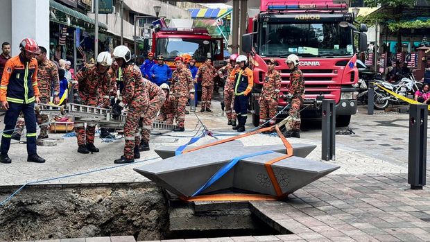 Pemadam Kebakaran dan Penyelamatan Malaysia ini menunjukkan petugas penyelamat memasuki lubang pembuangan yang dalam setelah menerima laporan bahwa seorang wanita terjatuh ke dalam lubang pembuangan setelah satu bagian trotoar ambruk di Kuala Lumpur, Jumat, 23 Agustus 2024. (AP Photo/Vincent Thian)